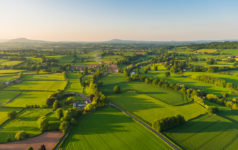 Warm sunset light illuminating the picturesque patchwork quilt landscape of green pasture, agricultural crops, farms and villages below clear blue panoramic skies.