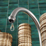 Water droplet dripping from a kitchen water tap surrounded by stacks of gold coins with green rectangular tiles as background. Illustration of the relationship between pipe leakage and money