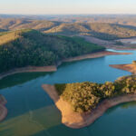 This aerial drone image showcases Mount Bold Reservoir Dam, the largest reservoir in South Australia, nestled within the picturesque Adelaide Hills. The footage captures the expansive forested landscape, winding waterways, and the massive dam wall from a high vantage point. Surrounded by protected catchment zones and scenic lookouts, the area is known for its vital role in water storage and stunning natural beauty.