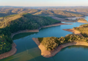 This aerial drone image showcases Mount Bold Reservoir Dam, the largest reservoir in South Australia, nestled within the picturesque Adelaide Hills. The footage captures the expansive forested landscape, winding waterways, and the massive dam wall from a high vantage point. Surrounded by protected catchment zones and scenic lookouts, the area is known for its vital role in water storage and stunning natural beauty.