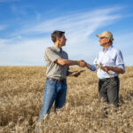 Wide full length view of agricultural engineer shaking hands with farmer while giving practical advice for season's harvest