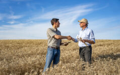 Wide full length view of agricultural engineer shaking hands with farmer while giving practical advice for season's harvest