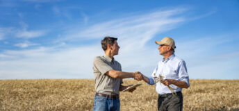 Wide full length view of agricultural engineer shaking hands with farmer while giving practical advice for season's harvest